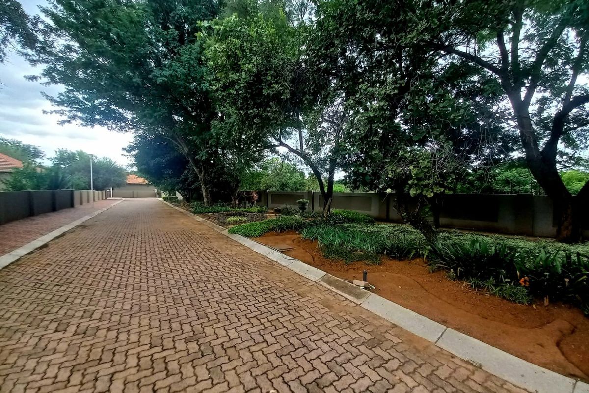 A well-maintained residential driveway featuring interlocking brick paving, mature trees, and established garden beds along a perimeter wall.