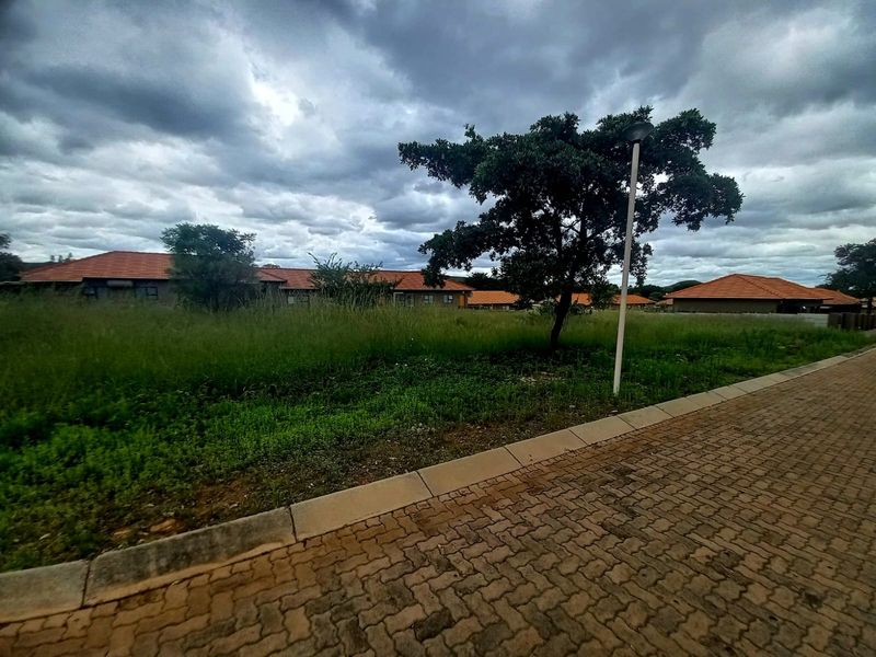 A vacant residential plot featuring a paved driveway, kerbing, and established street lighting, situated within a developed residential estate.
