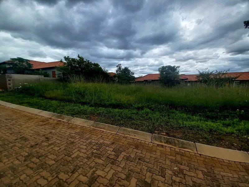 A vacant residential plot featuring a paved driveway, concrete curbing, and established boundary walls in a developed neighborhood setting.