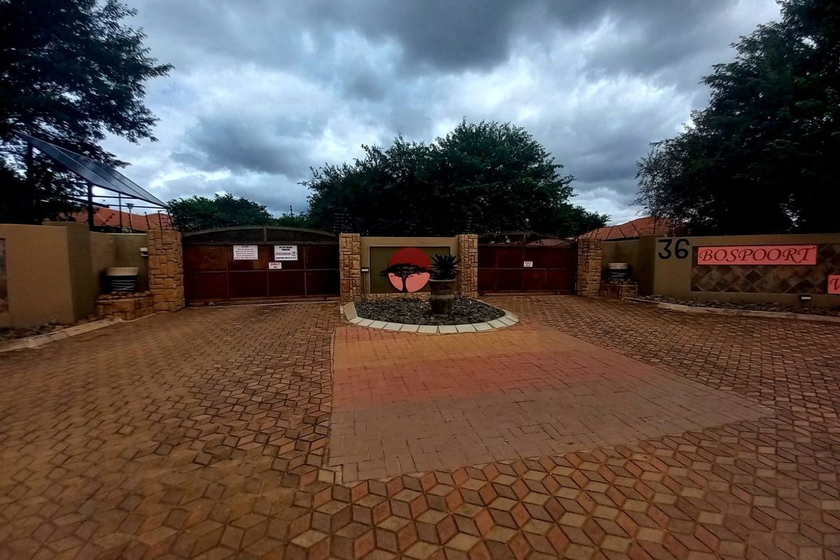 Front entrance view of the residential property featuring a paved driveway, secure perimeter wall, and gated access.