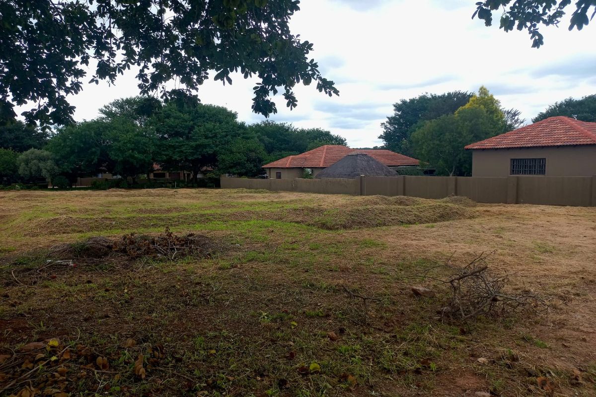 A view of a vacant residential plot featuring cleared grass and a perimeter boundary wall, situated in a developed neighborhood.