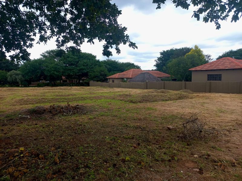 A view of a vacant residential plot featuring cleared grass and a perimeter boundary wall, situated in a developed neighborhood.