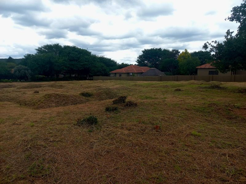 A vacant residential plot featuring uneven terrain and a perimeter boundary wall, offering a blank canvas for future development.