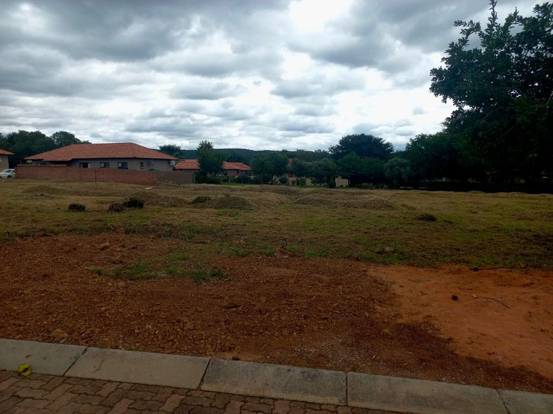 A vacant residential plot of land featuring cleared grass and soil, situated in a developed neighborhood with surrounding residential properties.