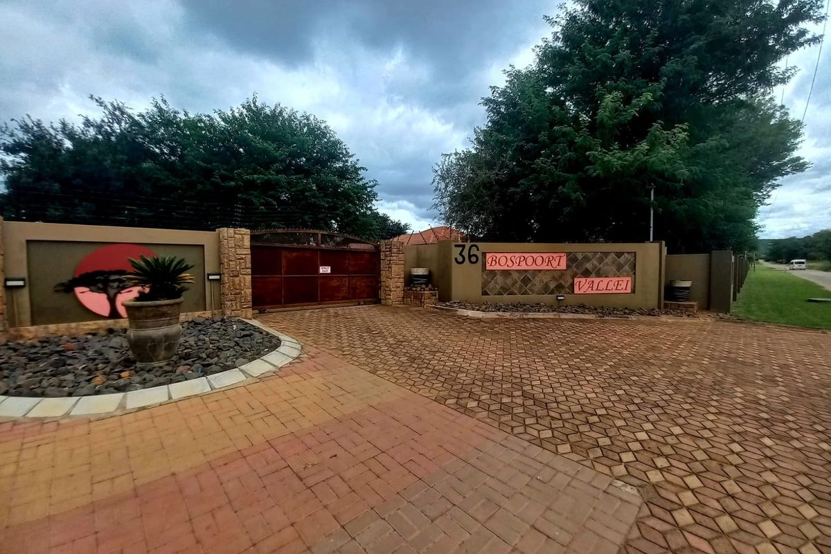 Front entrance view of the property featuring a paved driveway, secure metal gate, perimeter wall with electric fencing, and decorative stone cladding.