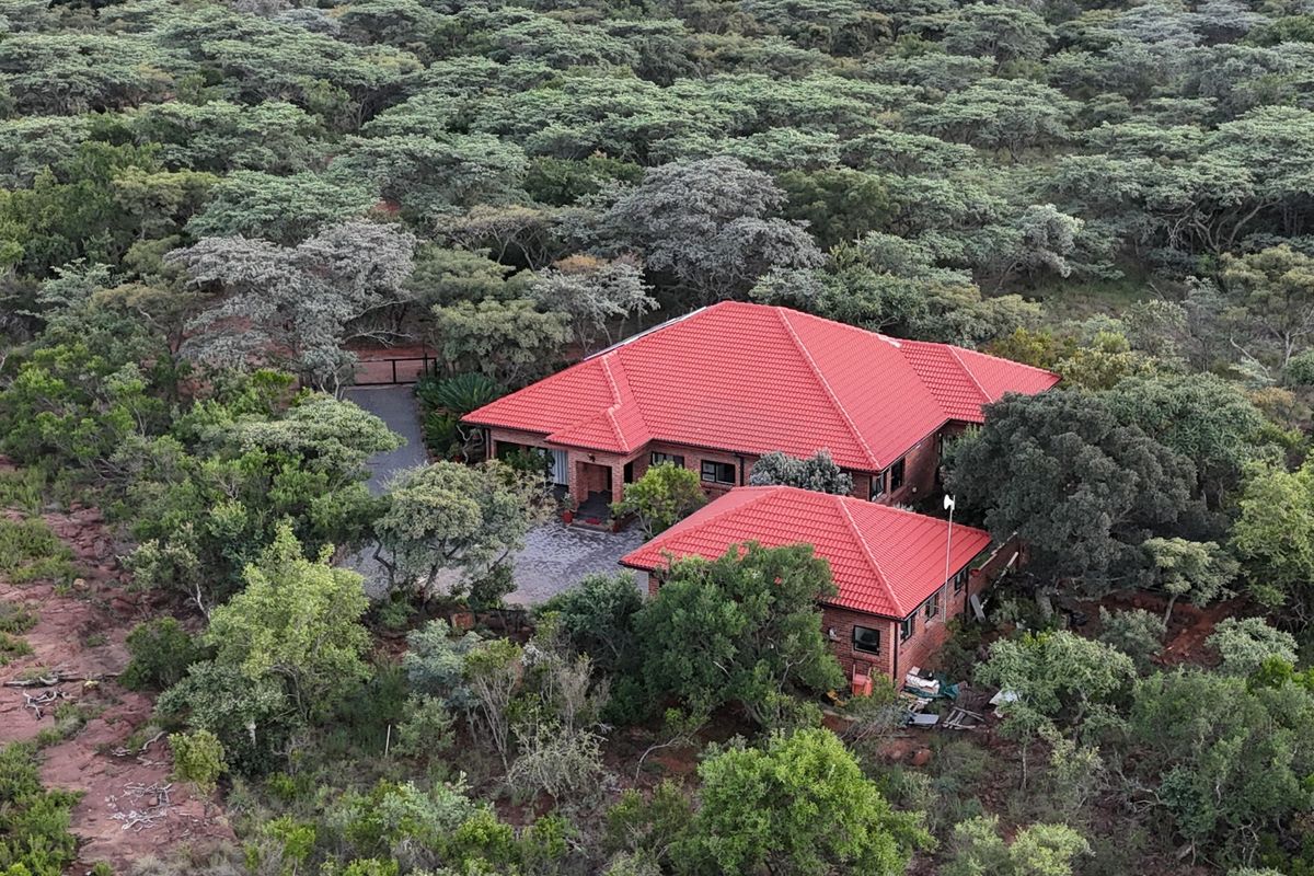 Aerial view of a brick house with a red tiled roof, nestled within a dense, natural wooded landscape.