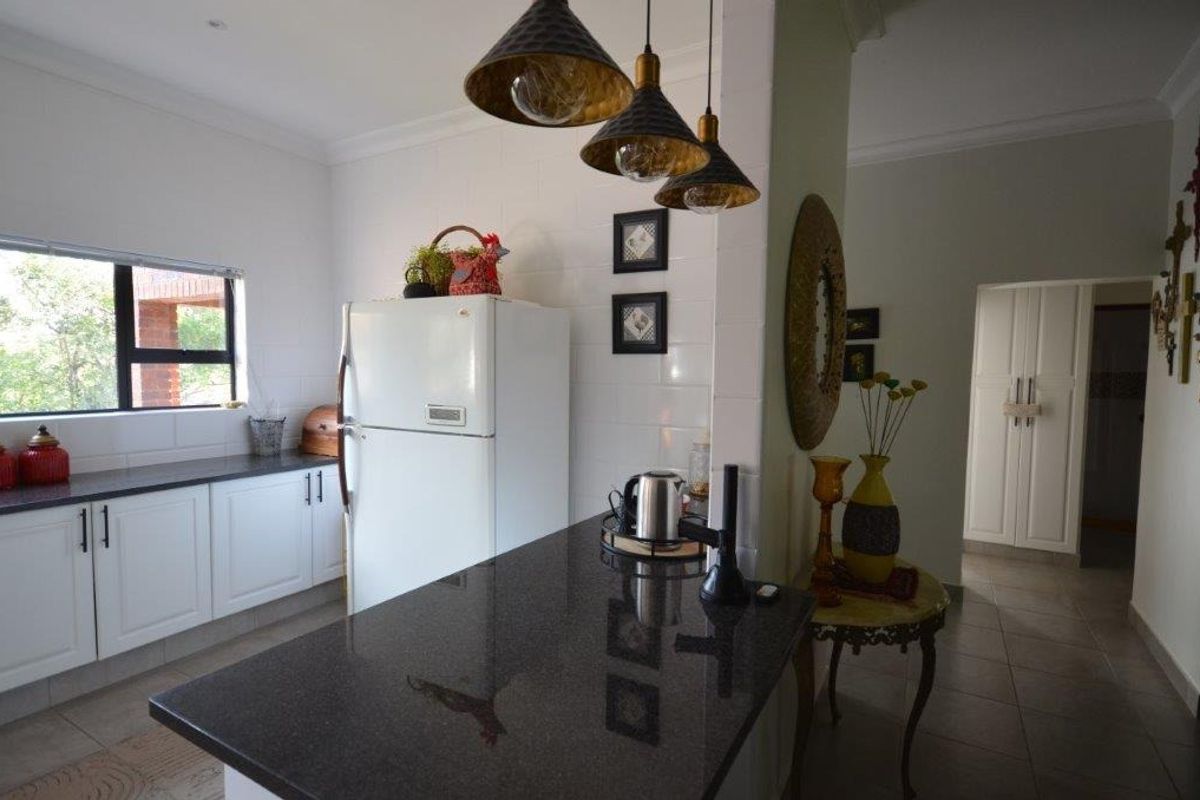 A functional kitchen featuring granite countertops, white cabinetry, and modern pendant lighting, with an open flow into the adjacent hallway area.