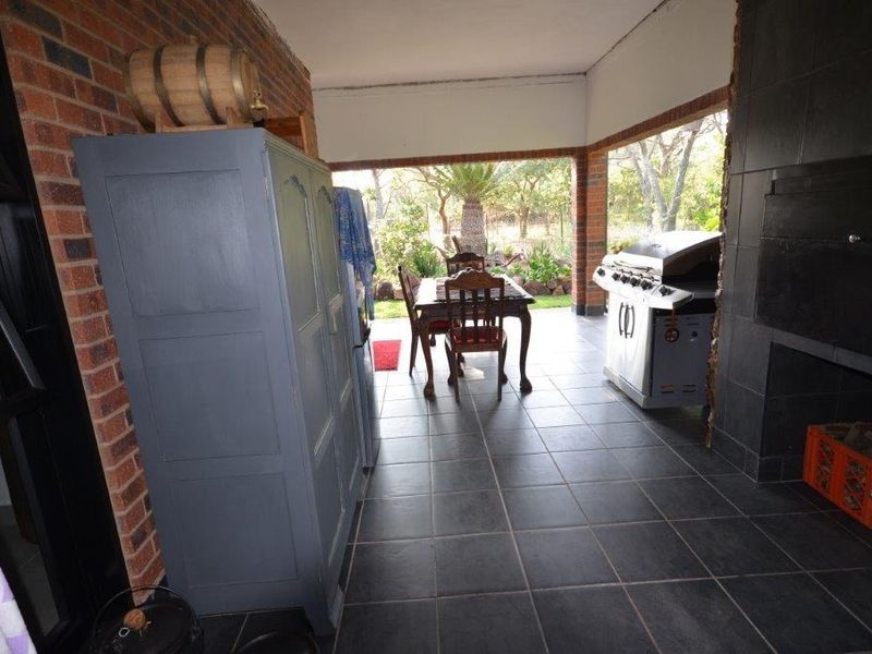 Covered patio area featuring tiled flooring, an exposed brick wall, and a built-in braai, providing a functional outdoor entertainment space overlooking the garden.