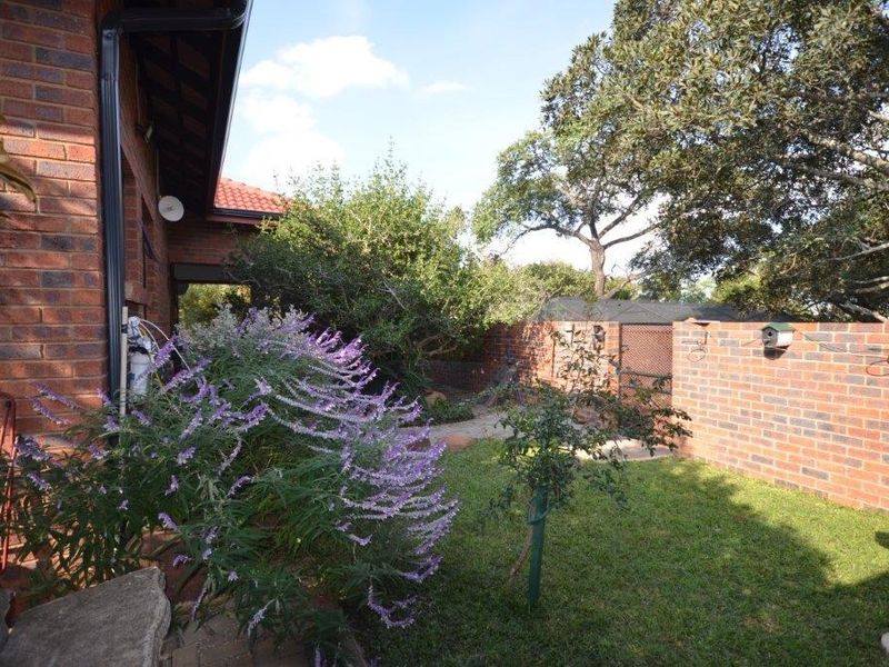 A view of the rear garden featuring a face brick exterior wall, paved pathways, and established trees and shrubs.