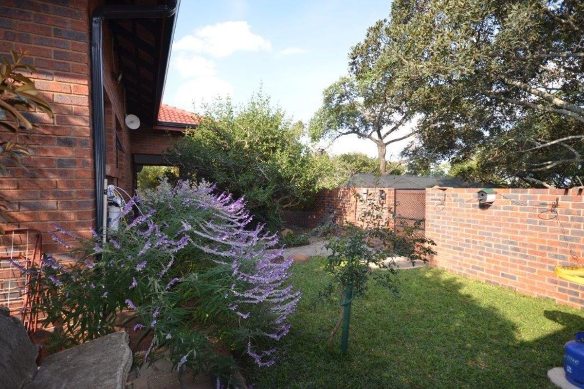 A view of the rear garden featuring a face brick exterior wall, paved pathways, and established trees and shrubs.