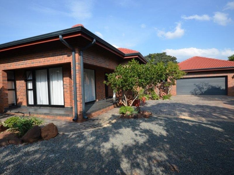 A well-maintained face brick house featuring a tiled roof, paved driveway, and a double garage with a covered patio entrance.