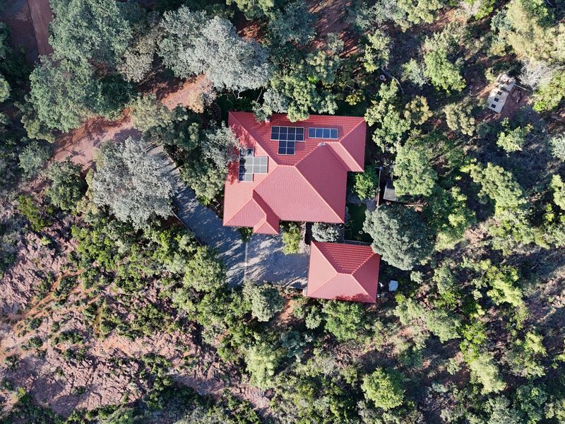 Aerial view of a residential property featuring a tiled roof with integrated solar panels, surrounded by mature trees and a paved driveway.