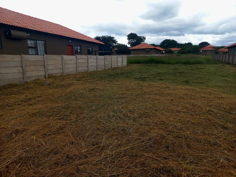 A view of the rear yard area featuring a precast concrete boundary wall and adjacent residential structures with tiled roofs.