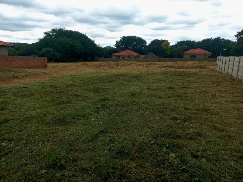 A vacant residential plot featuring cleared grass, enclosed by brick and precast concrete boundary walls in a quiet neighborhood setting.