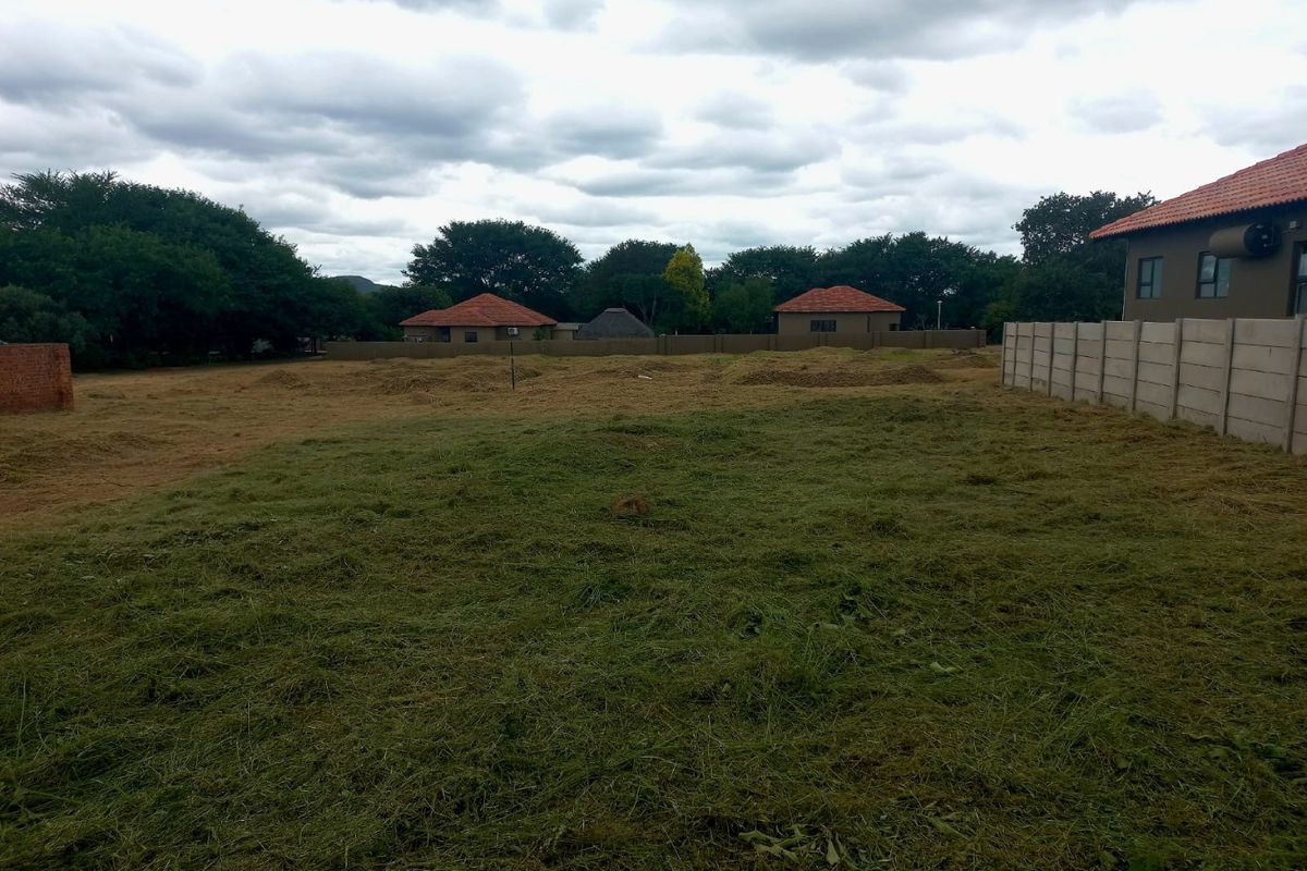 A view of a cleared, vacant residential plot featuring a precast concrete boundary wall and surrounding neighborhood homes.