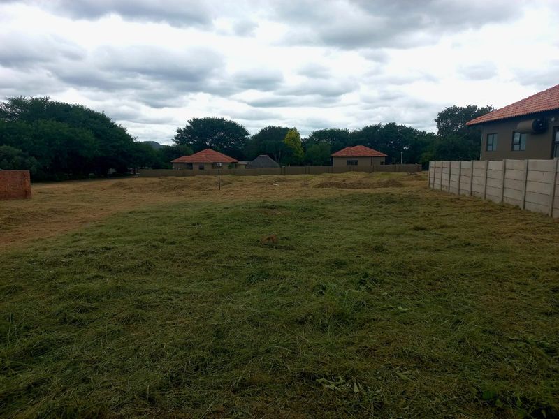 A view of a cleared, vacant residential plot featuring a precast concrete boundary wall and surrounding neighborhood homes.