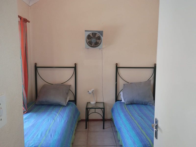 A compact bedroom featuring tiled flooring and a wall-mounted ventilation fan.