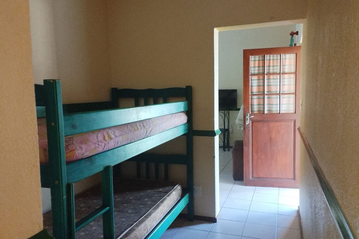 A bedroom featuring tiled flooring and a wooden door leading to an adjacent living area, with a chair rail detail along the walls.