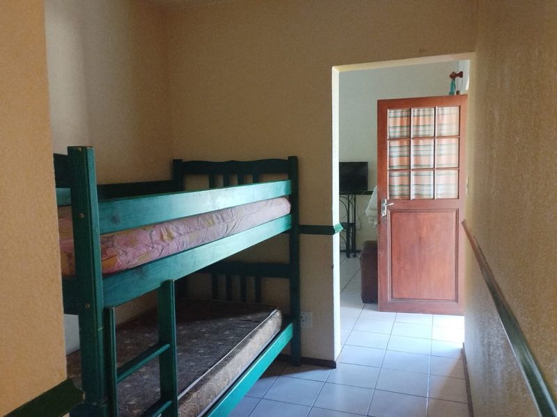 A bedroom featuring tiled flooring and a wooden door leading to an adjacent living area, with a chair rail detail along the walls.
