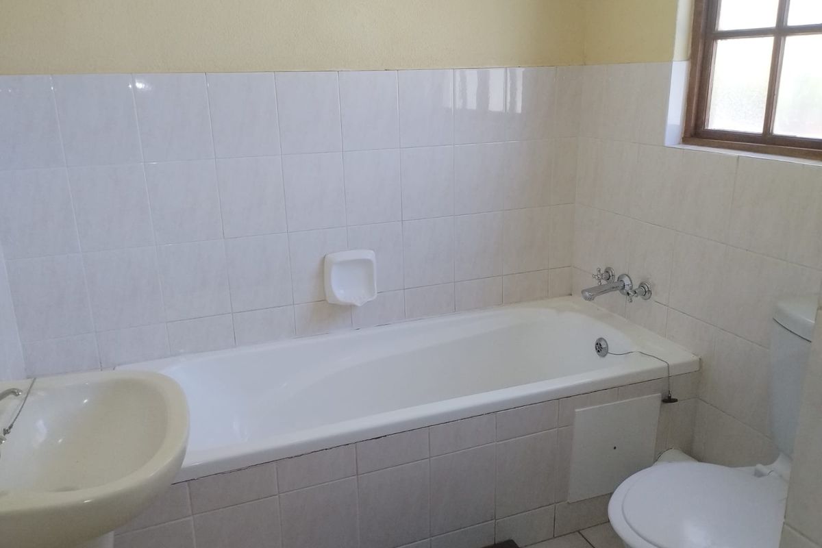 A functional bathroom featuring a standard bathtub, pedestal basin, and toilet with tiled walls and natural light from a window.