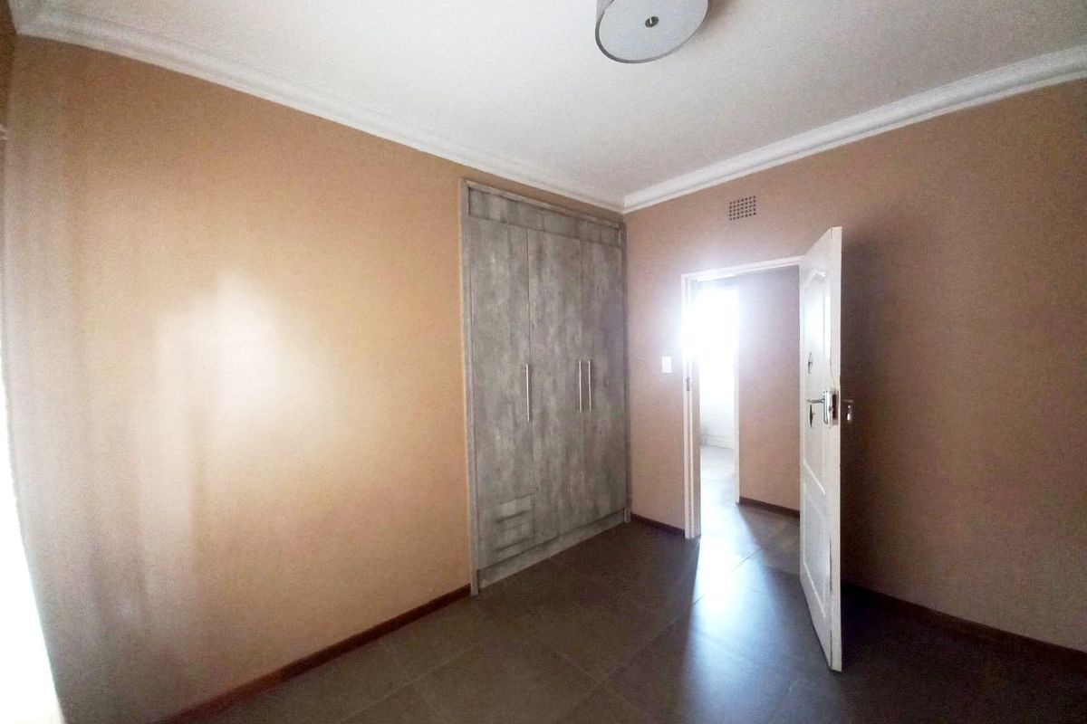 A clean, empty bedroom featuring neutral wall tones, modern tiled flooring, and built-in cupboards, offering a versatile space ready for personalization.