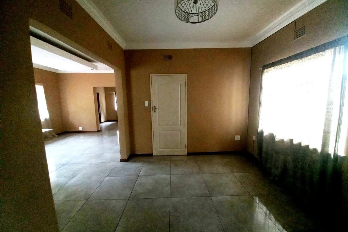 An empty living room featuring neutral wall tones, large format floor tiles, and a central light fixture, offering a blank canvas for interior design.