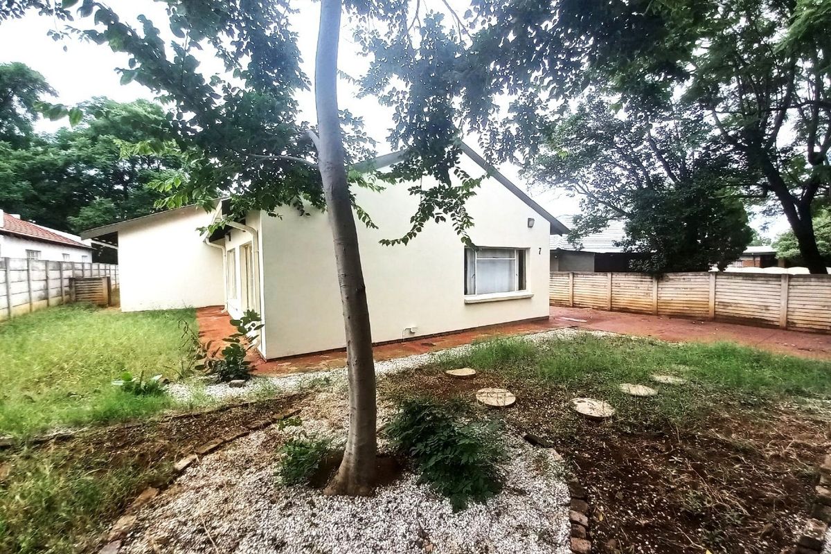 Rear view of the property featuring a paved patio area, perimeter walling, and a garden space with mature trees.