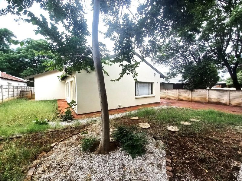 Rear view of the property featuring a paved patio area, perimeter walling, and a garden space with mature trees.