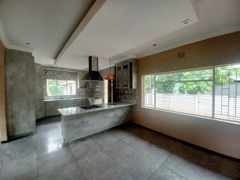 Modern kitchen featuring a central island with a gas cooktop, stone countertops, mosaic backsplash, and ample built-in cabinetry with recessed ceiling lighting.