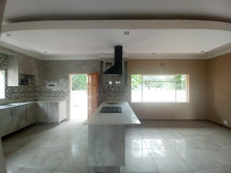 Spacious kitchen featuring a central island with a gas hob, extractor fan, ample cabinetry, and large windows providing natural light.