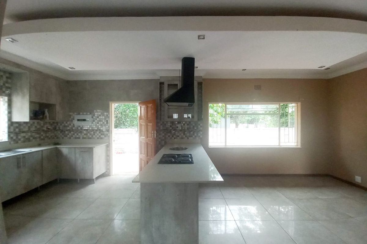 Spacious kitchen featuring a central island with a gas hob, extractor fan, ample cabinetry, and large windows providing natural light.