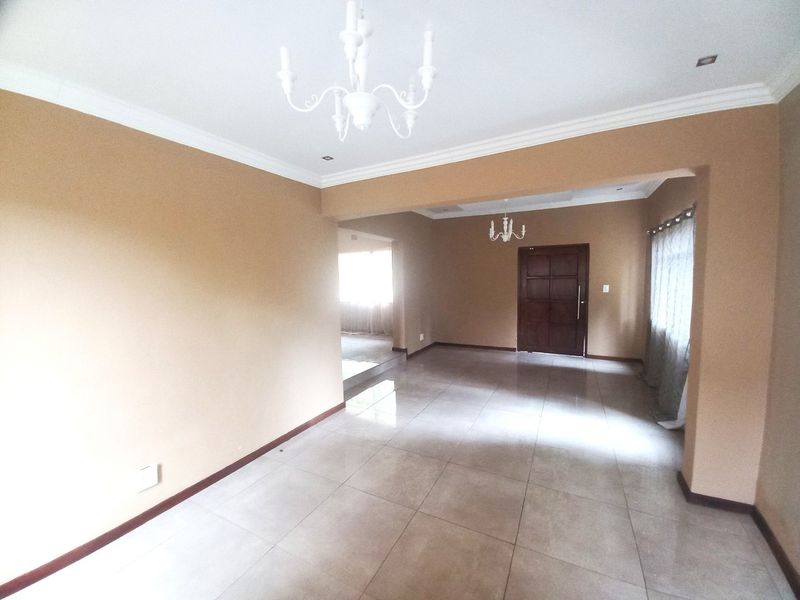 Spacious open-plan living area featuring neutral wall tones, large format floor tiles, crown molding, and elegant chandeliers throughout the connected interior spaces.