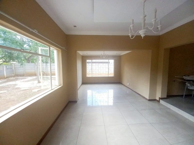 Spacious open-plan living area featuring neutral wall tones, large windows with security bars, and polished tiled flooring throughout.
