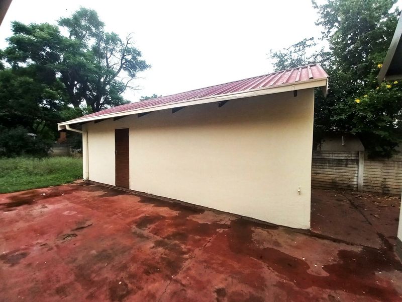 Rear view of a detached outbuilding featuring a corrugated metal roof, a single timber door, and a weathered concrete patio area.