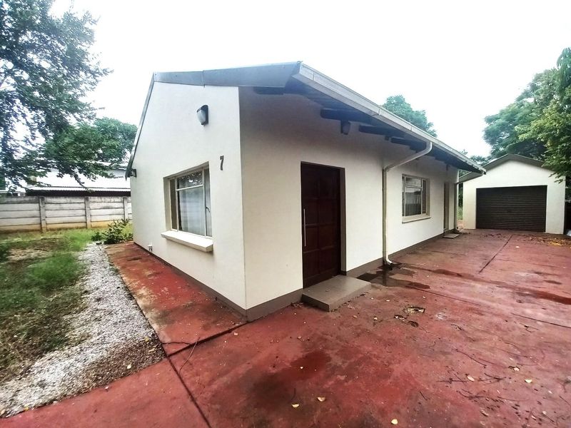 Front view of a single-story house featuring a concrete driveway, detached garage, and perimeter walling.