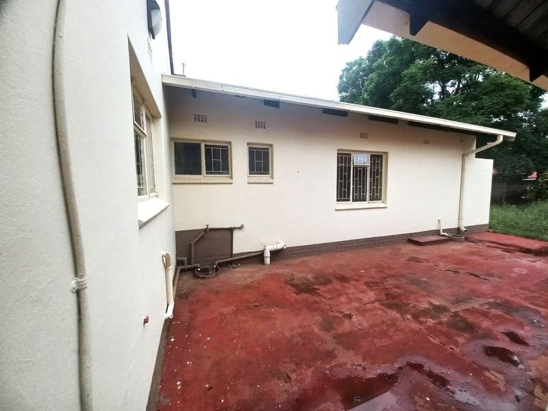 Rear exterior view of the property featuring a concrete patio area, security-barred windows, and exposed external plumbing fixtures.