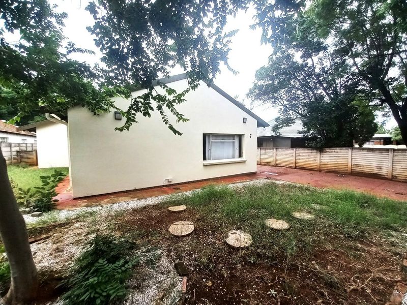 Rear view of the property featuring a paved area, precast boundary wall, and a garden space requiring maintenance.