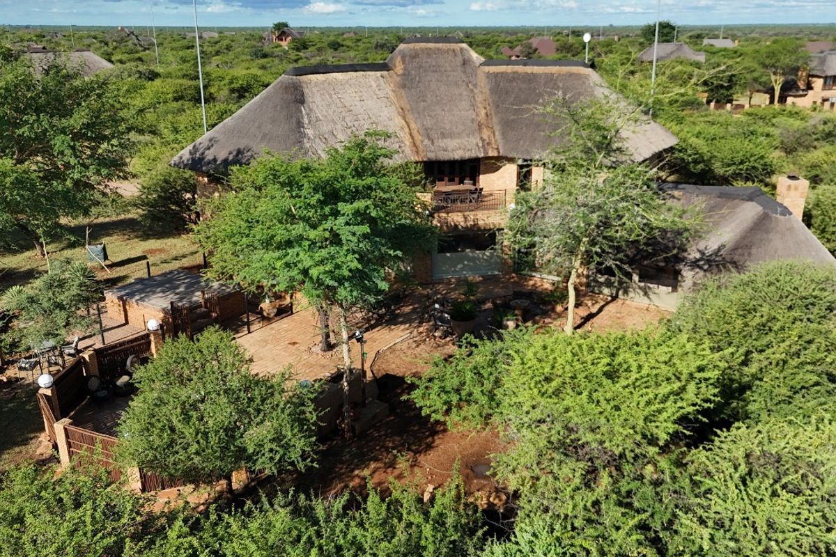 Aerial view of a guest house property featuring a traditional thatch roof, brick patio area, and surrounding natural bushveld landscape.