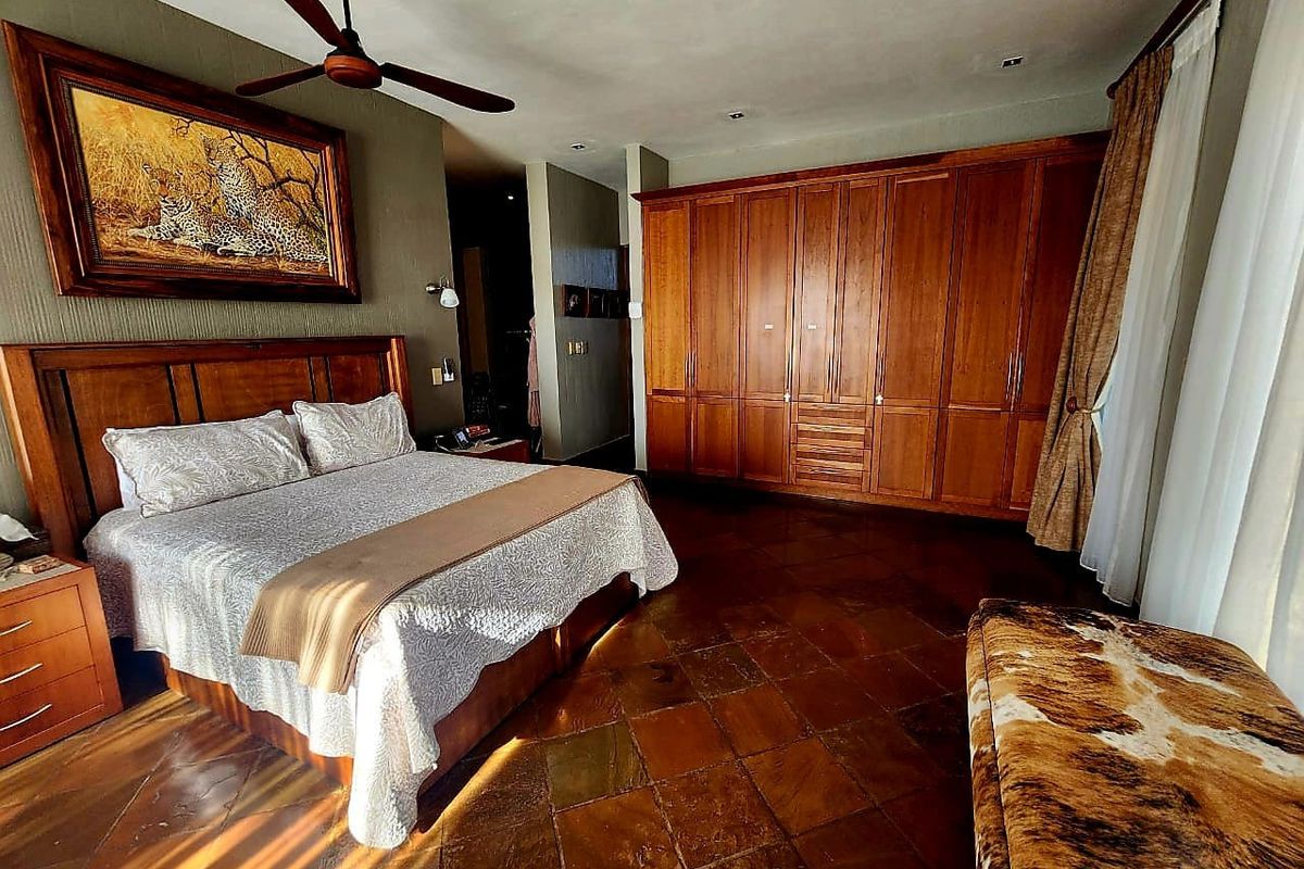 Spacious bedroom featuring extensive built-in wooden cabinetry, tiled flooring, and a ceiling fan, offering a warm and functional living space.