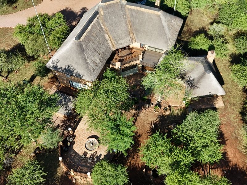 Aerial view of a guest house property featuring a traditional thatched roof, paved patio area, and surrounding natural landscape.