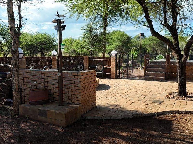 An outdoor patio area featuring brick paving, brick boundary walls with reed fencing, and integrated outdoor lighting, set within a natural garden environment.