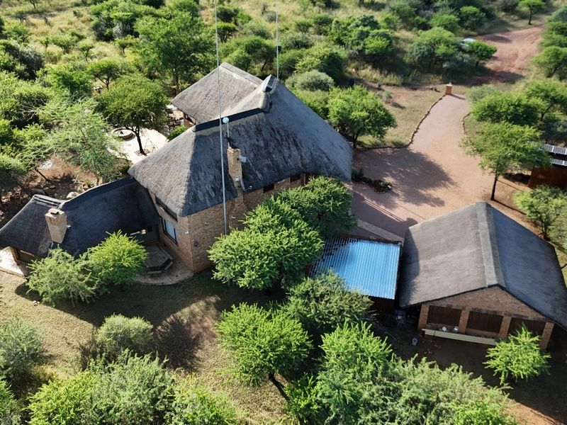 Aerial view of a bushveld guest house property featuring multiple structures with traditional thatch roofing, brick exteriors, and a surrounding natural landscape.