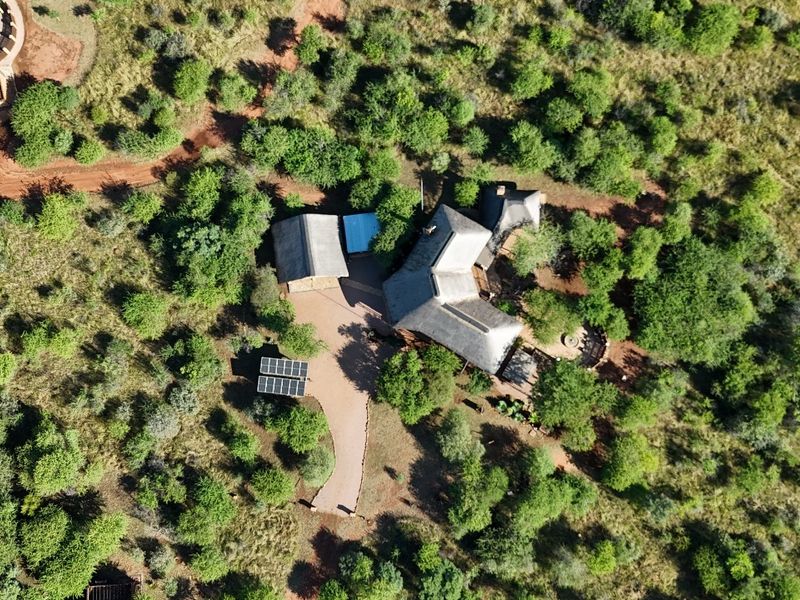 Aerial view of the guest house property featuring multiple thatched roof structures, a driveway, and solar panel installation set within a natural bushveld landscape.