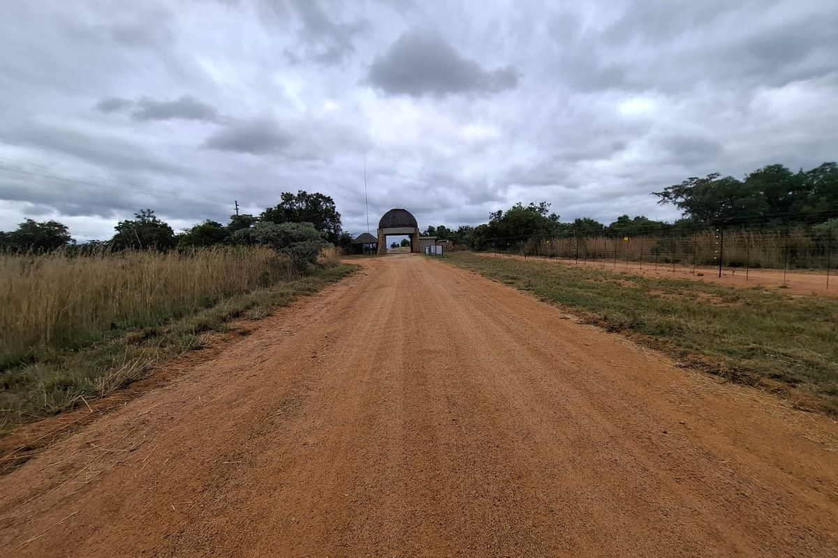 A view of a dirt access road leading towards a gated entrance structure on a vacant residential property.