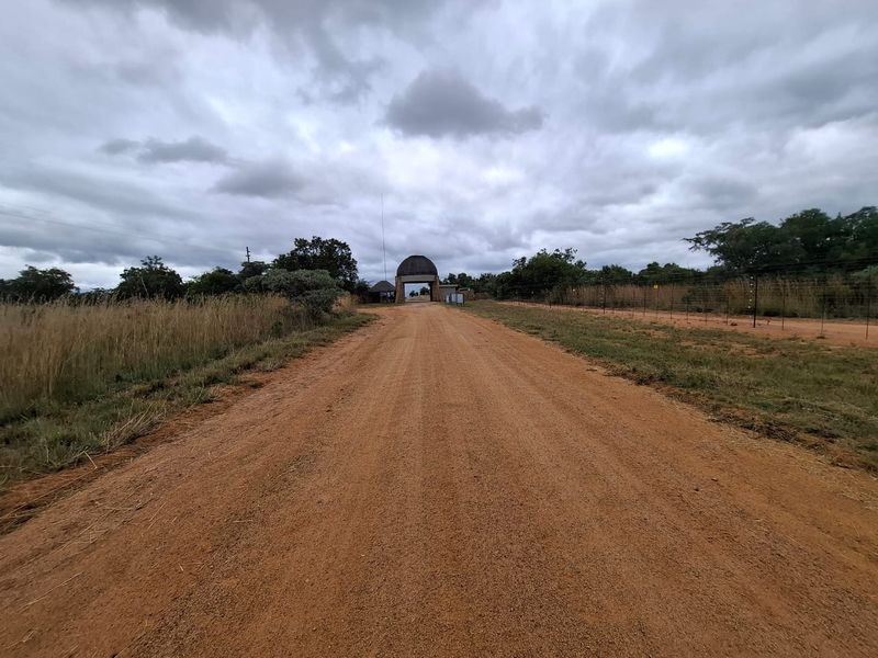 A view of a dirt access road leading towards a gated entrance structure on a vacant residential property.
