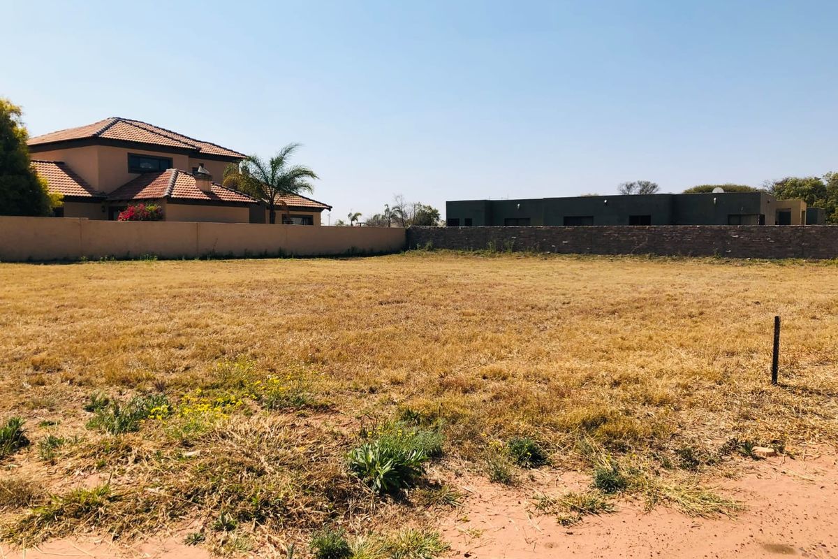 A vacant residential plot of land featuring dry grass, enclosed by perimeter walls and boundary fencing in a developed neighborhood.