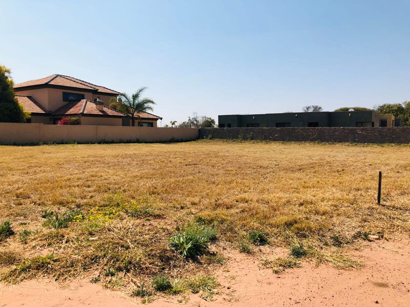 A vacant residential plot of land featuring dry grass, enclosed by perimeter walls and boundary fencing in a developed neighborhood.