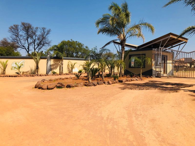 Front entrance view of the residential estate featuring a security gate, guard house, and landscaped perimeter wall.