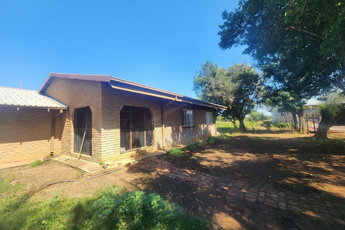 Rear view of a facebrick small holding dwelling featuring a metal roof, security bars on windows, and a brick pathway leading through the garden area.