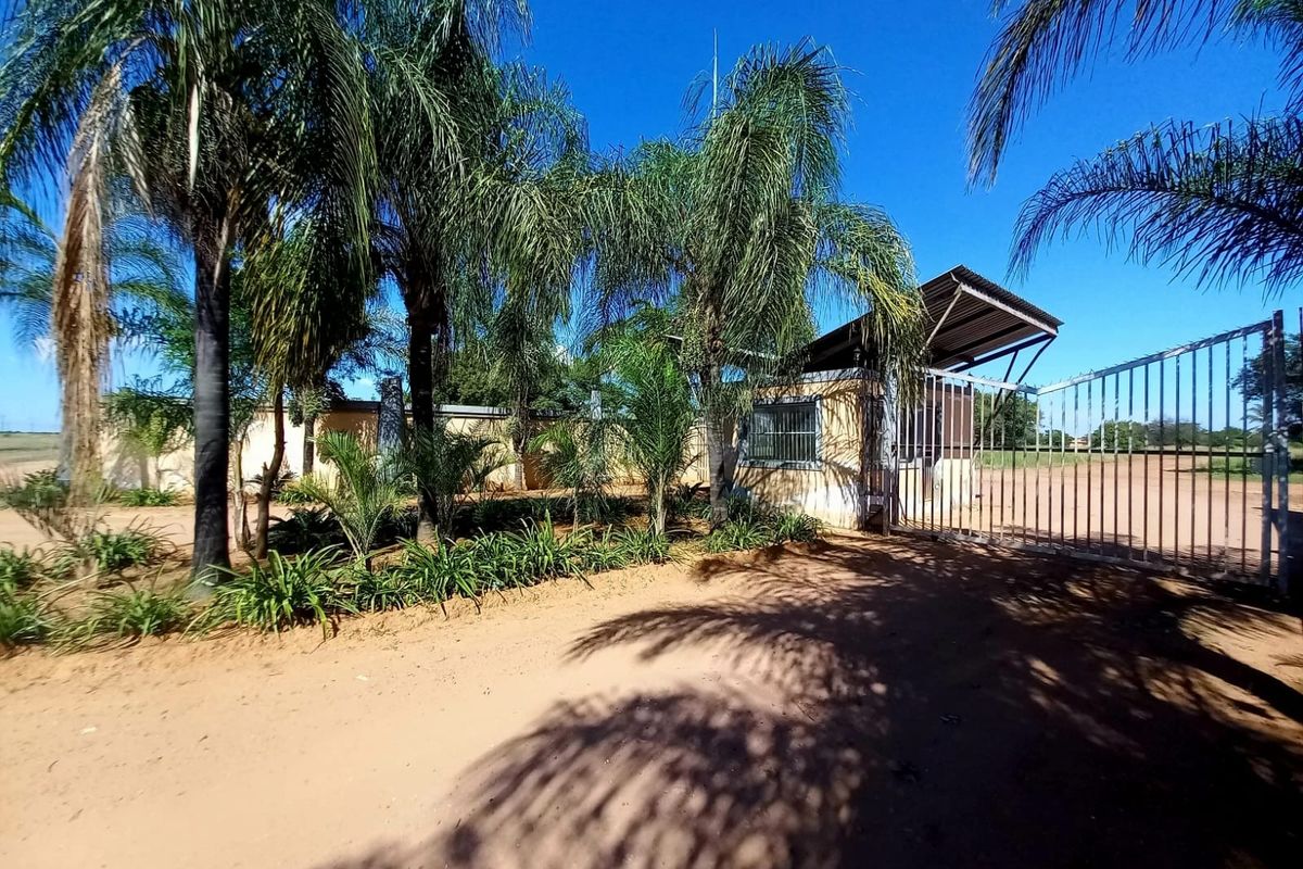 Front entrance view of the property featuring a metal security gate, perimeter wall, and a small guard house structure.